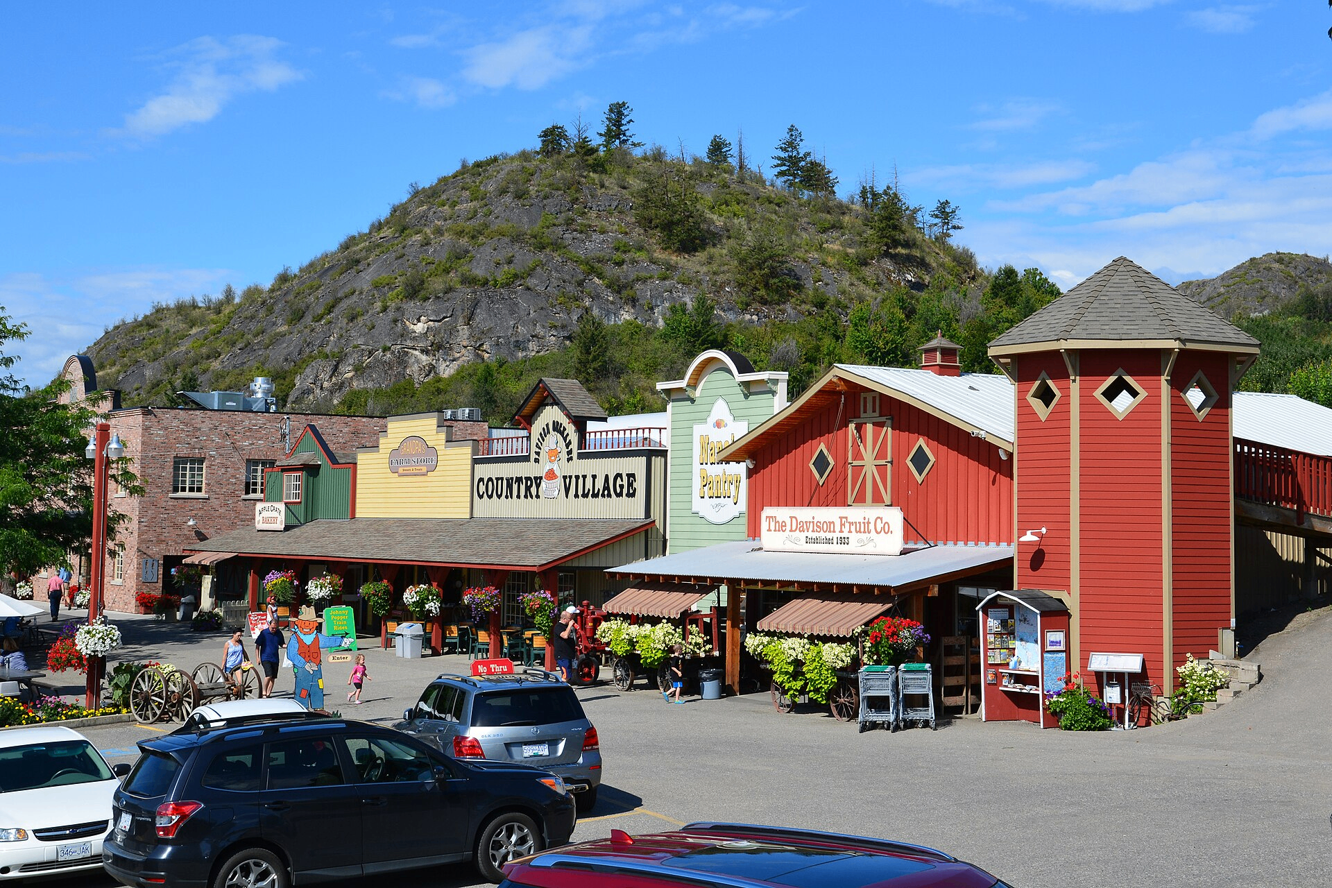 Davison Orchards Country Village in Vernon — red and yellow barns against a rocky hillside under blue Okanagan sky
